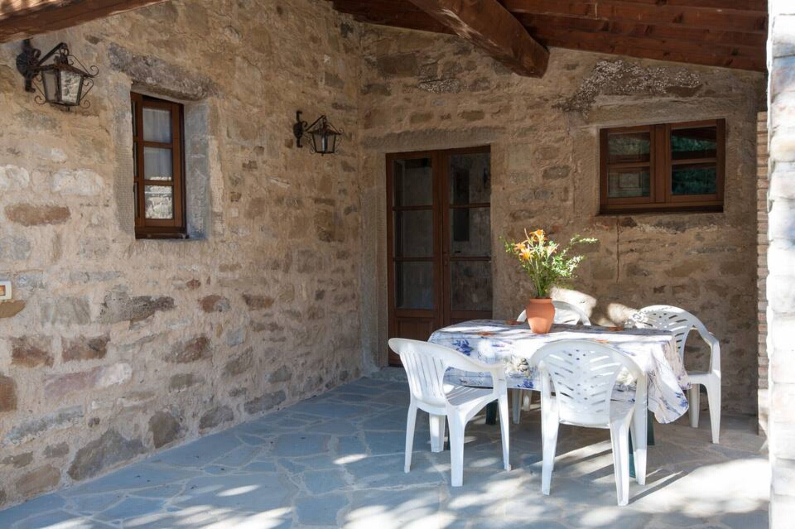 A stone building with a wooden ceiling, a table with chairs, and a potted plant.
