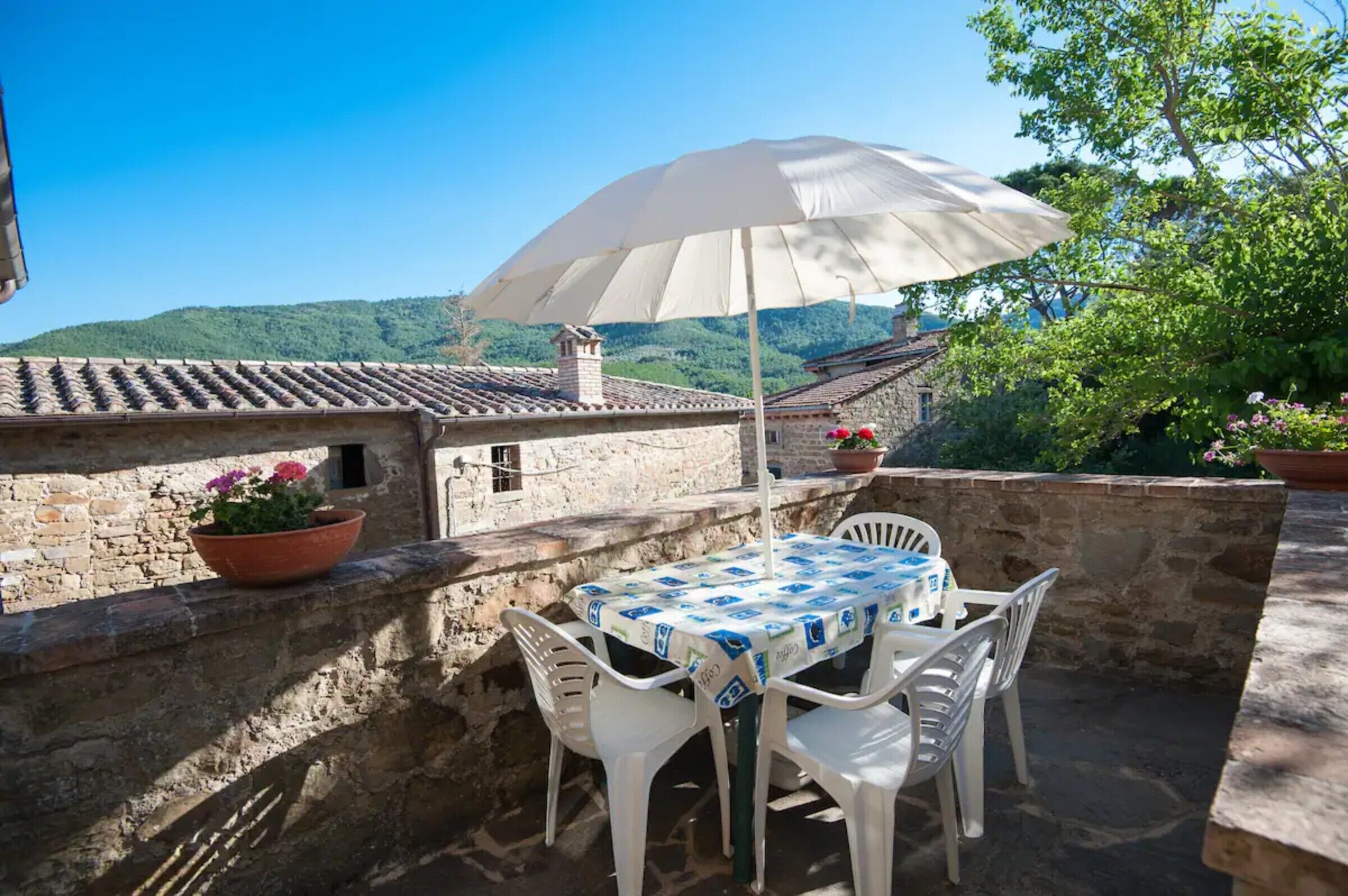 Eine Terrasse im Freien mit Tisch, Stühlen, einem weißen Sonnenschirm und Blumentöpfen.