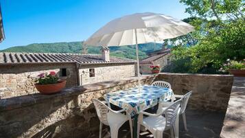 Eine Terrasse im Freien mit Tisch, Stühlen, einem weißen Sonnenschirm und Blumentöpfen.