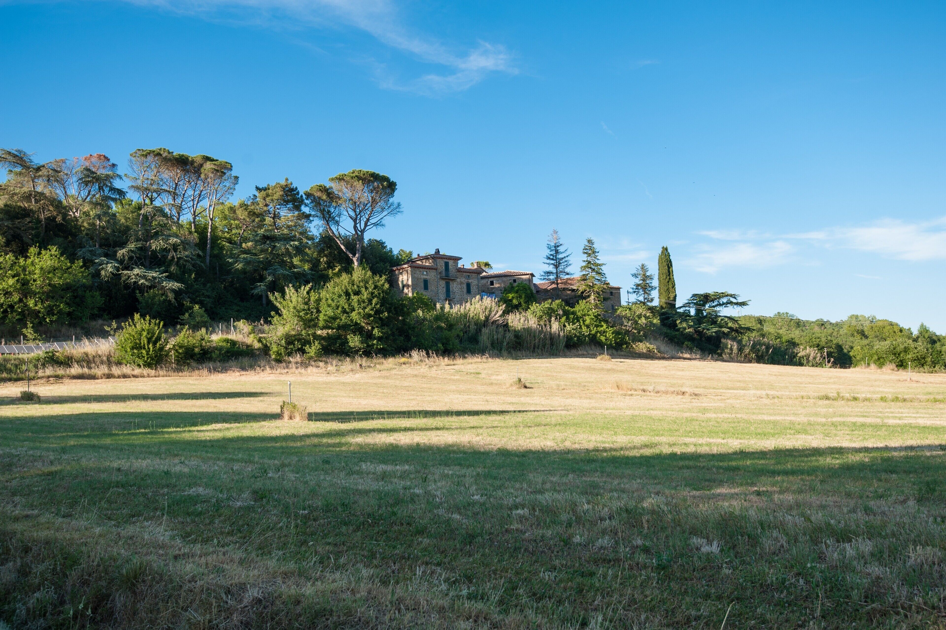 A rural landscape with a stone building surrounded by trees and open fields.