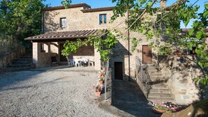 A stone building with a tiled roof, a gravel driveway, and a small patio area with outdoor seating. - Farmhouse "Pilari Appartamento Stalla" with Shared Pool, Private Terrace & Wi-Fi (Cortona)