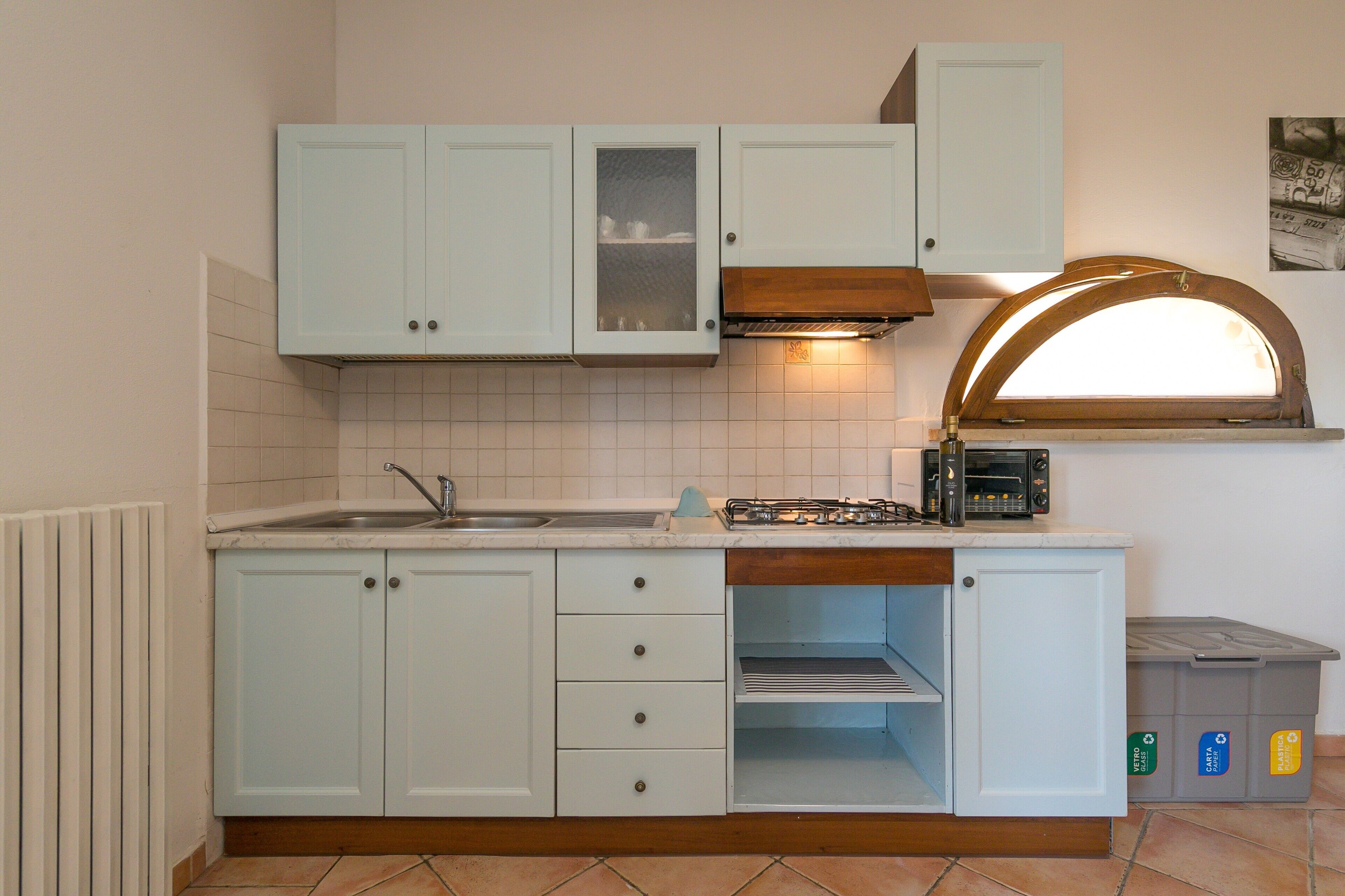A kitchen with light blue cabinets, a gas stove, a sink, and a trash bin.
