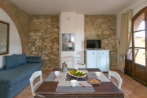 A dining area with a stone wall, a sofa, a TV, and a dining table set with plates, cups, and a bottle.