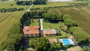 Une grande maison avec une piscine, entourée de champs et d’arbres.
