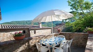 A stone terrace with a table and chairs, an umbrella, and potted plants. - Apartment "Pilari Castagnolo" with Mountain View, Shared Pool & Wi-Fi (Cortona)
