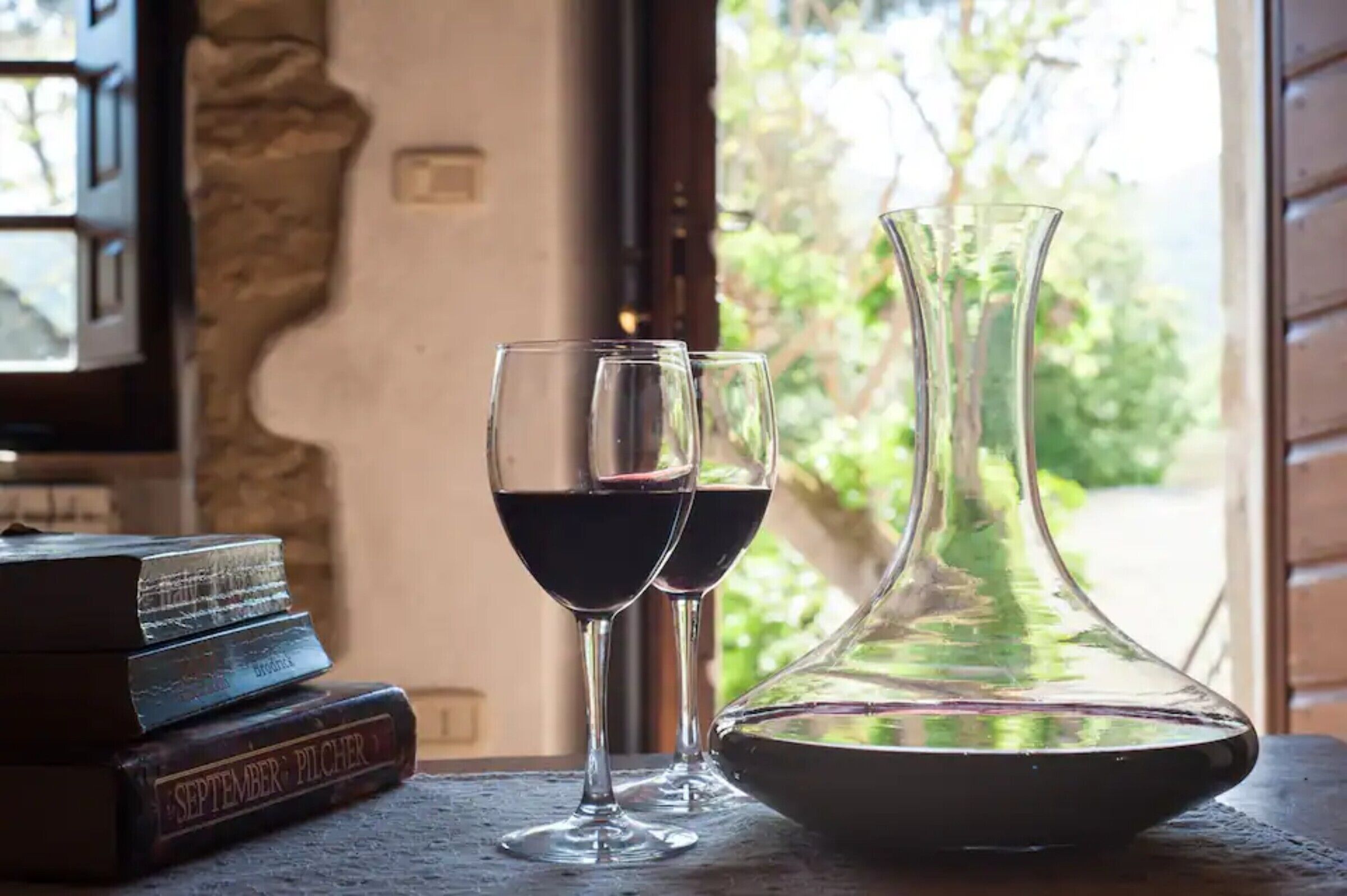 Una mesa con dos copas de vino, un libro titulado 'SEPTEMBER: PITCHER' y un florero de vidrio transparente.