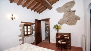 A bedroom with a bed, a wooden desk, a chair, a stone wall, and a window. - Apartment "Pilari Castagnolo" with Mountain View, Shared Pool & Wi-Fi (Cortona)