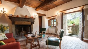 A cozy room with a fireplace, a dining table, chairs, and a view through an open door. - Apartment "Pilari Castagnolo" with Mountain View, Shared Pool & Wi-Fi (Cortona)