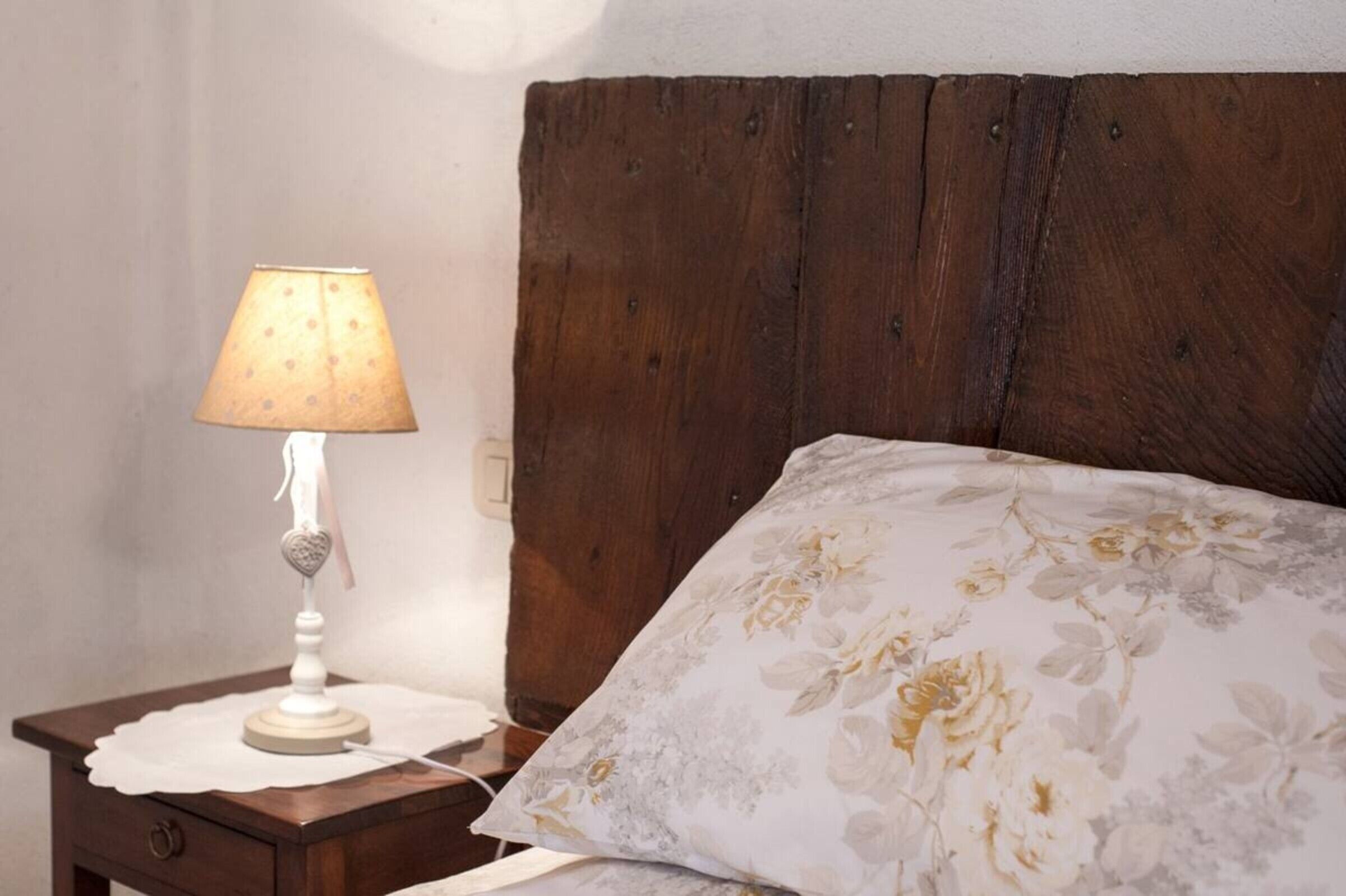 A bed with a floral pillow, a wooden headboard, and a bedside table with a lamp.