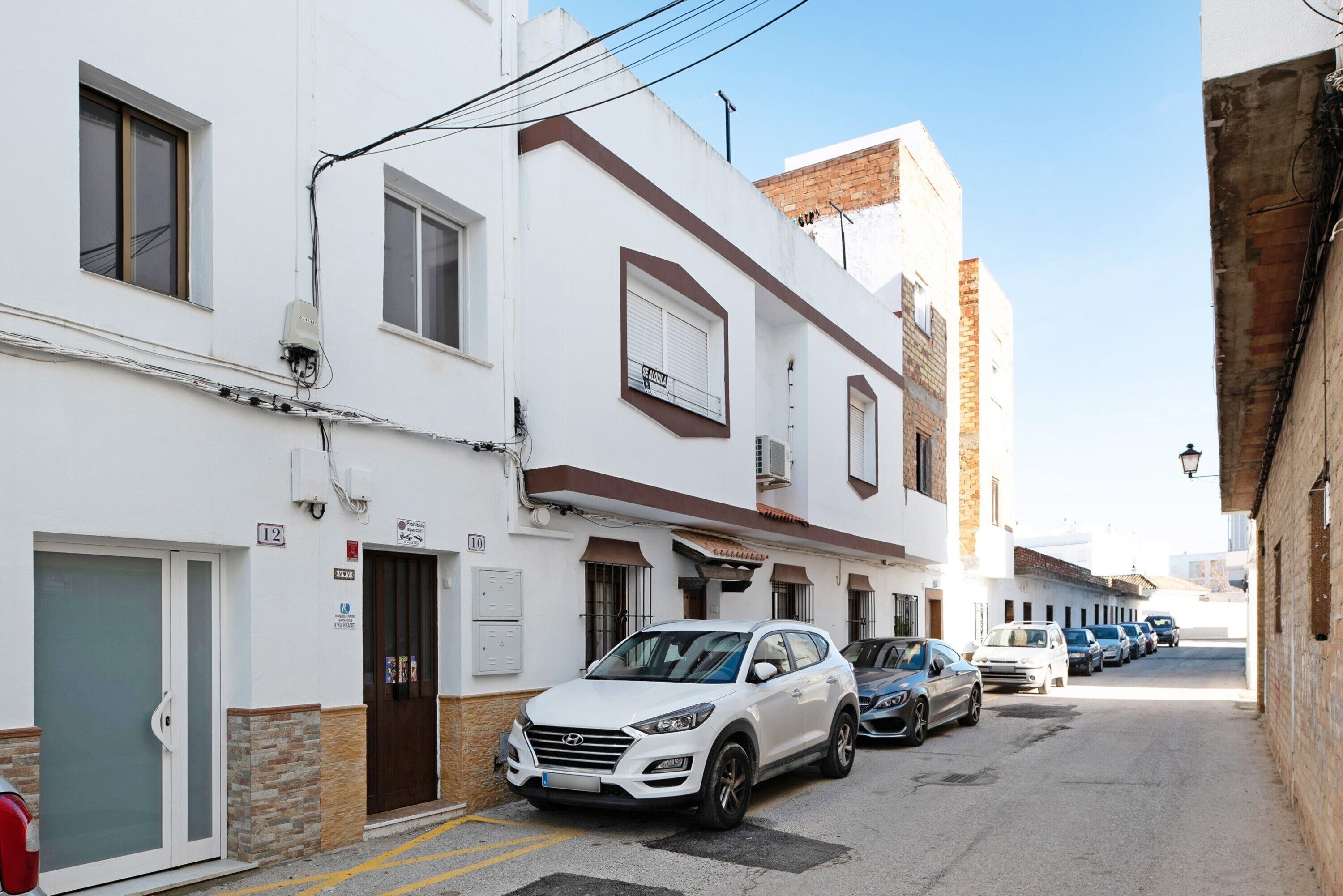 Una calle estrecha con edificios blancos, coches aparcados e hidrante.