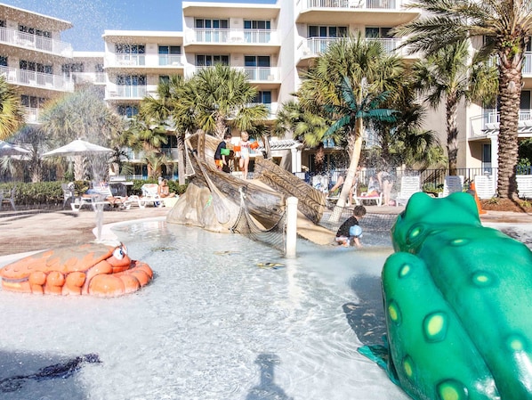 A water park area with a slide, palm trees, and a pool.