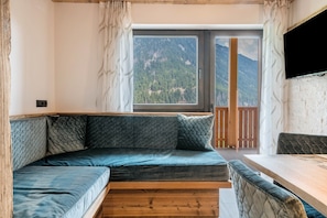 A modern interior with a curved sofa, a wooden dining table, and a large window offering a mountain view.
