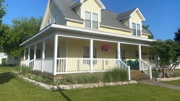 A two-story house with a covered porch and a stone border. - The Yellow House-Three bedroom within walking distance of Lake Michigan. (Ludington)