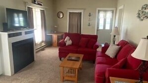 A living room with a red sofa, a wooden coffee table, and a television on a stand. - The Yellow House-Three bedroom within walking distance of Lake Michigan. (Ludington)