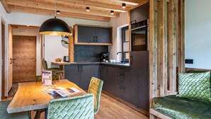 Eine kompakte Küche mit modernen Geräten, ein Essbereich mit Holztisch und -stühlen sowie eine gemütliche Sitzecke mit einem grünen Polstersofa.