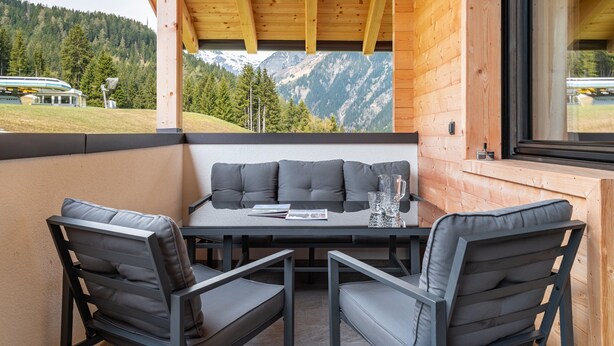 Un balcón de madera con un sofá, sillas, una mesa y vistas a las montañas.