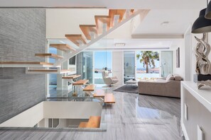 A modern interior with a glass staircase, a sofa, and a dining area.