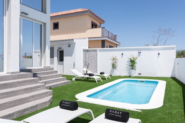 A modern pool area with steps leading to a pool, lounge chairs, and a building with a balcony.