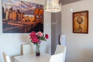 A dining area with a table, chairs, a vase of flowers, a cityscape painting, and a globe artwork on the wall.