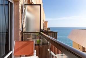 Un balcon avec vue sur la mer, une chaise, une table et une rambarde.