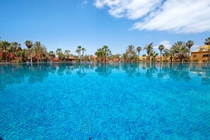 Ein klares, blaues Schwimmbecken mit Fliesenboden, umgeben von Palmen und Gebäuden.