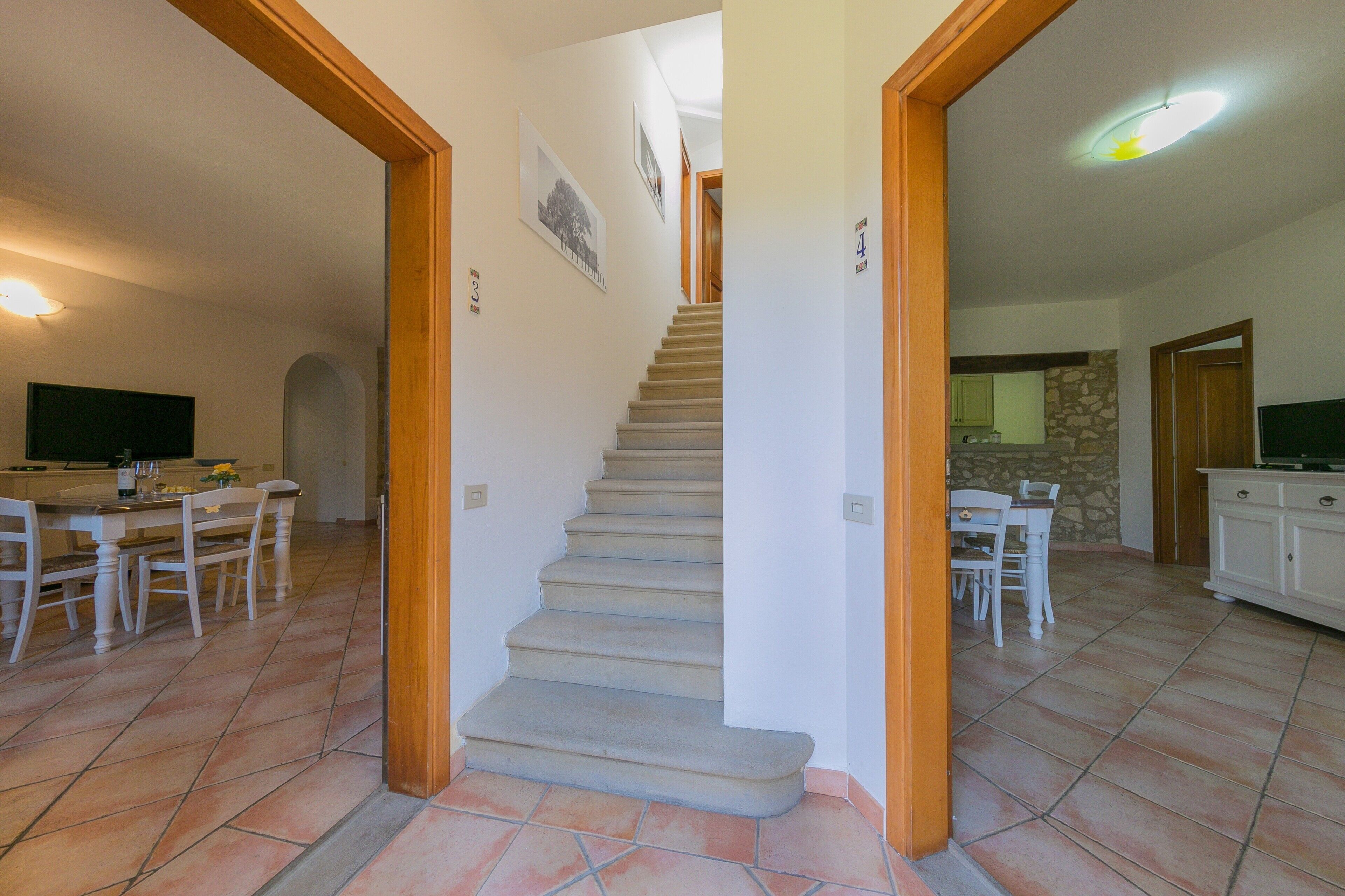 A staircase leading to a second floor, a dining area with a table and chairs, and a kitchen area with cabinets and a countertop.