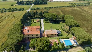 Vue aérienne d’une propriété comprenant un bâtiment principal, une piscine et des champs environnants.
