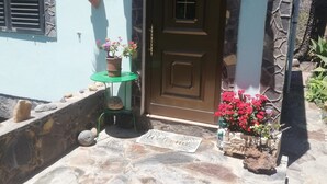 A house with a stone facade, a tiled roof, a brown door, and a small green table with potted plants. - Holiday Home "Casa Grenado" with Sea Views, Private Balcony & Wi-Fi (vallehermoso tazo)