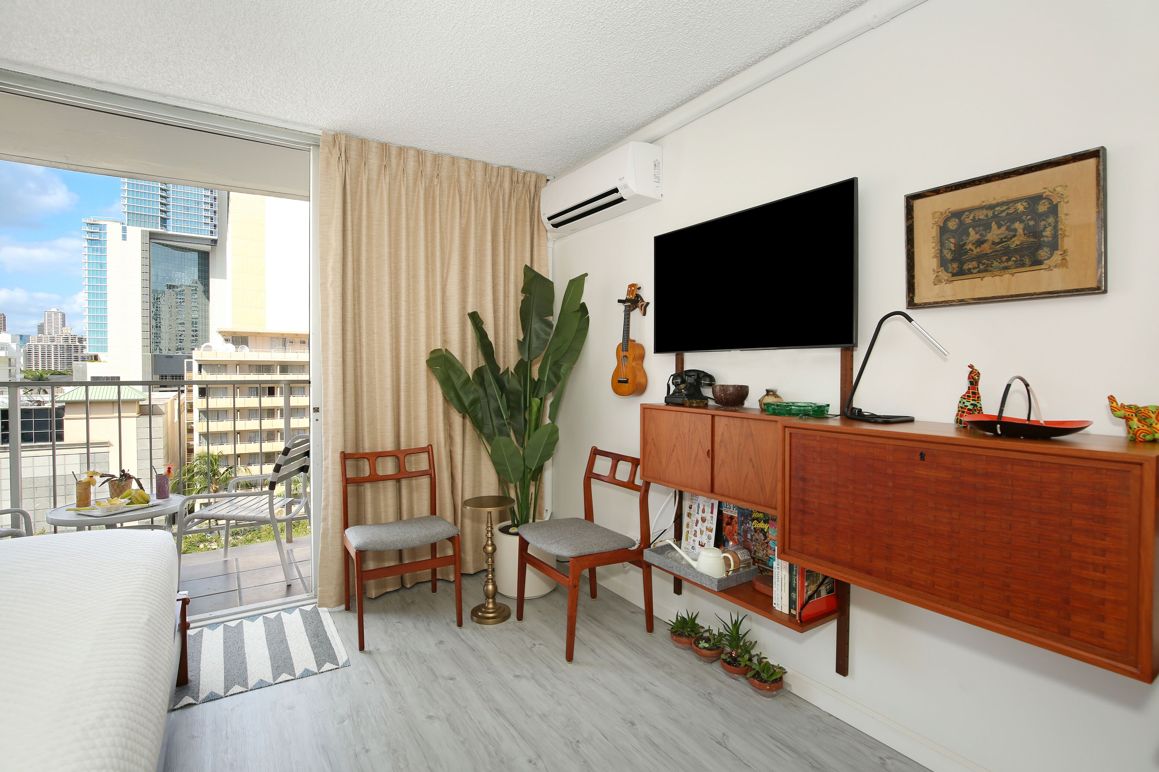 A hotel room with a balcony, a bed, a TV, a cabinet, and a large plant.