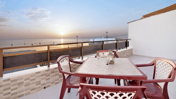 A terrace with a table and chairs, a view of the sea, and a sunset.