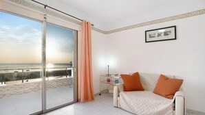 A room with a sliding glass door to a balcony, a sofa with cushions, a small bedside table, and a framed picture on the wall.