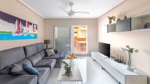 Un salon moderne avec un canapé gris, une table basse blanche, un téléviseur à écran plat et un ventilateur de plafond.