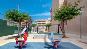 Un terrain de jeux avec deux balançoires et un toboggan, entouré d’arbres et de bâtiments.