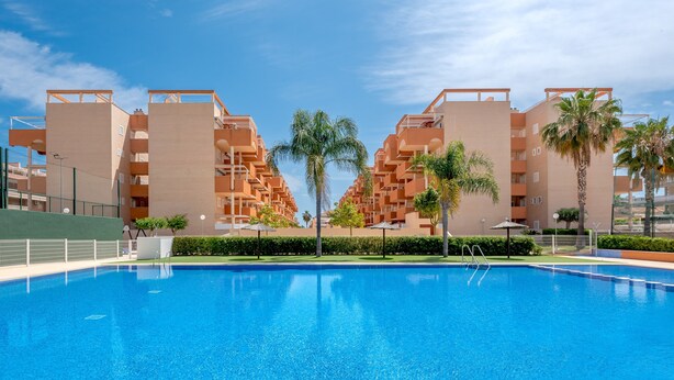 Une piscine à l’eau d’un bleu limpide, entourée d’immeubles d’appartements modernes dotés de balcons et de palmiers.