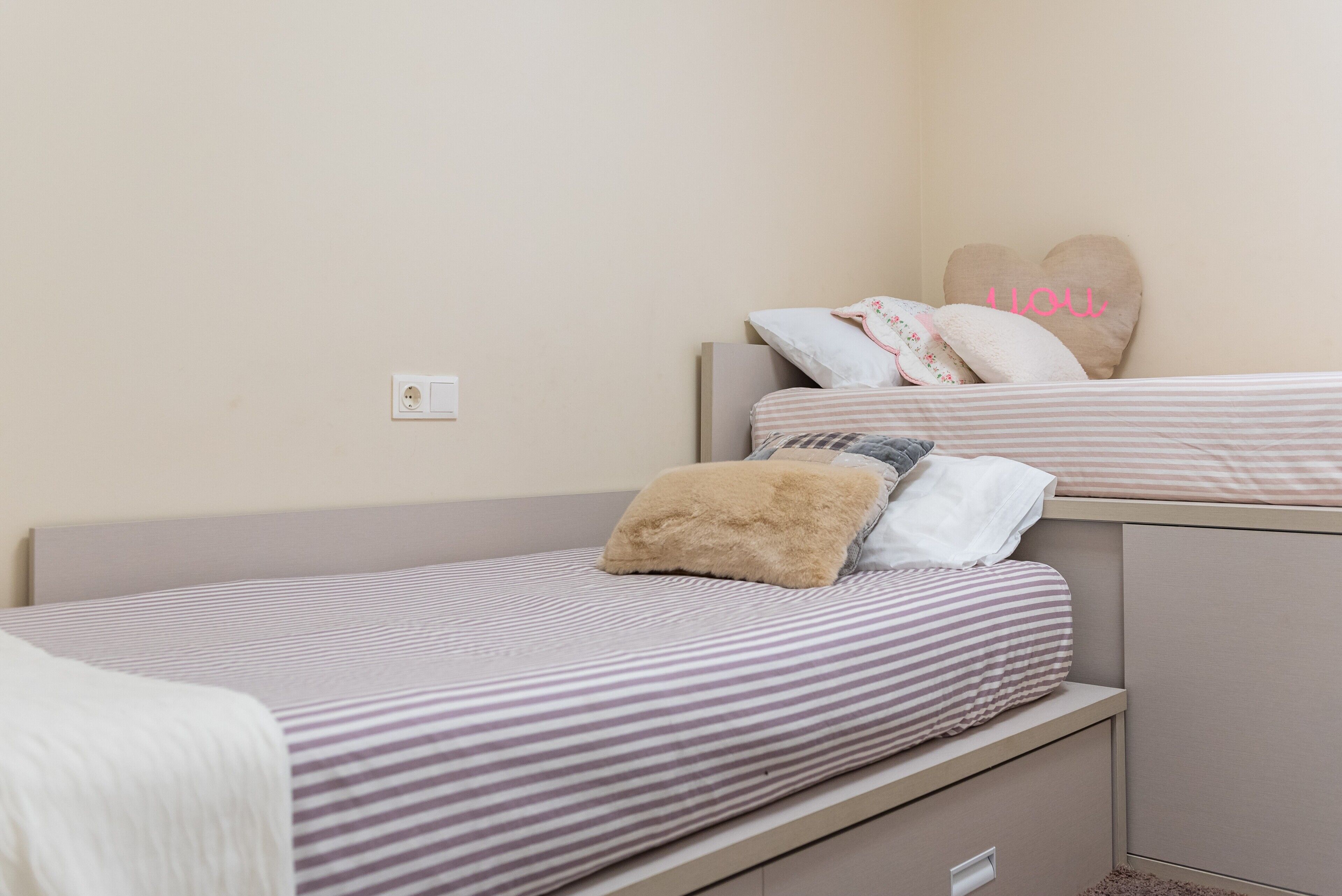 A single bed with striped bedding, a headboard, and a bedside drawer.