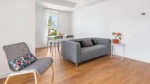 Un salon moderne avec un canapé gris, un fauteuil à motifs, une petite table sur laquelle est posée une plante en pot, et un coin repas avec des chaises et une table.