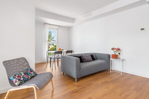Un salon moderne avec un canapé gris, un fauteuil à motifs, une petite table sur laquelle est posée une plante en pot, et un coin repas avec des chaises et une table.