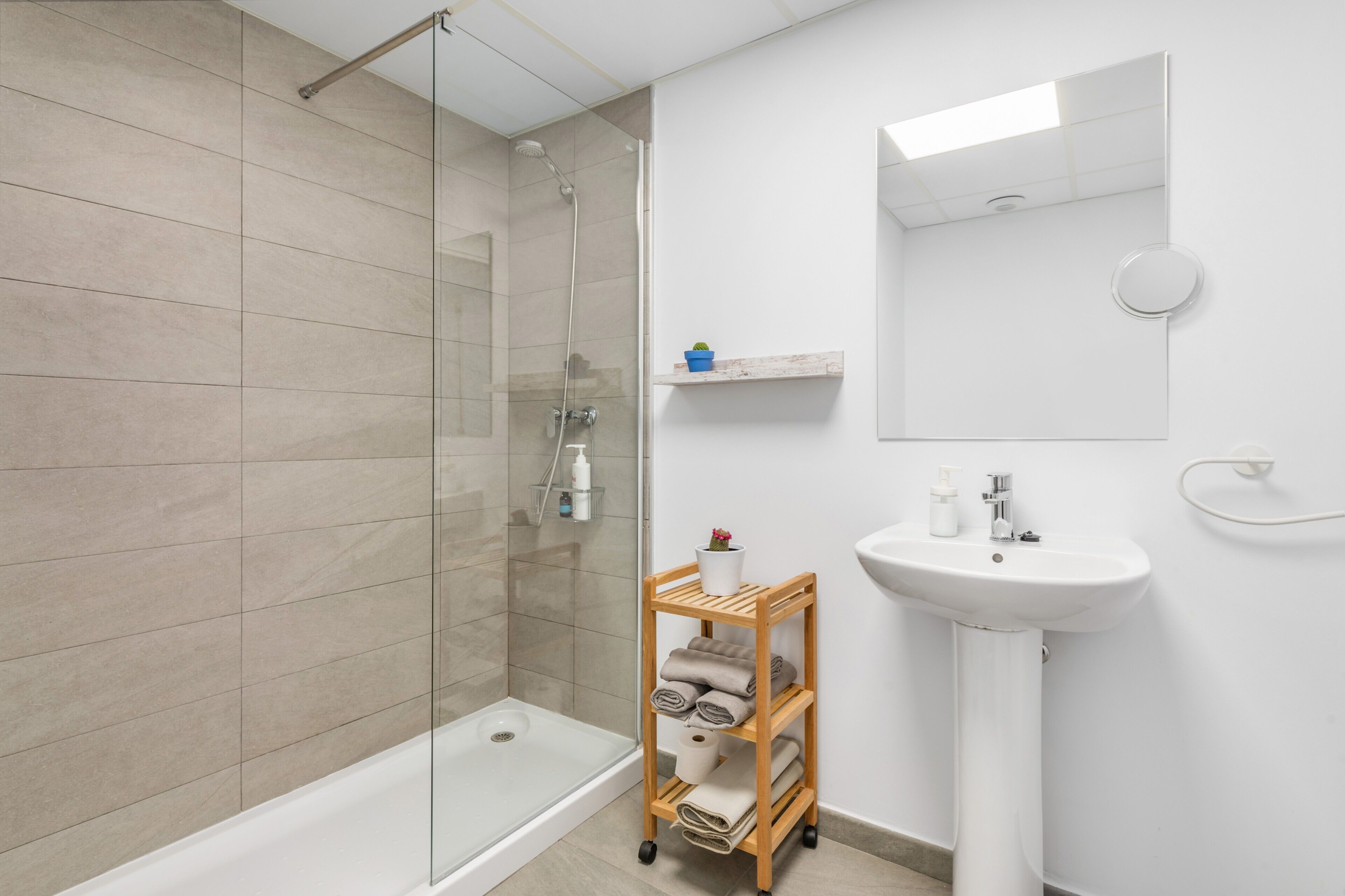A modern bathroom with a glass shower enclosure, a white pedestal sink, and a wooden towel rack.