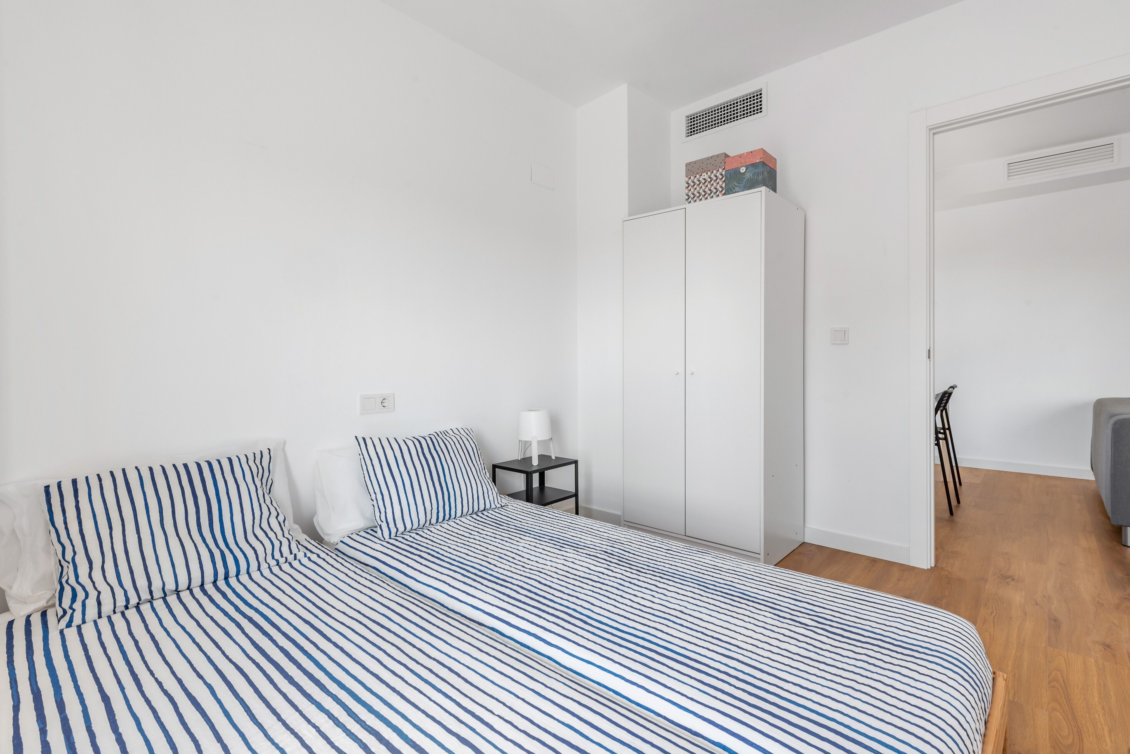 Un dormitorio con cama, mesita de noche, armario y una puerta.