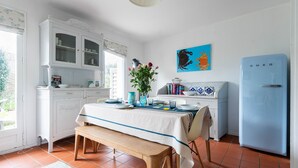 Una cocina con muebles blancos, un refrigerador azul y una mesa de comedor preparada para cuatro.