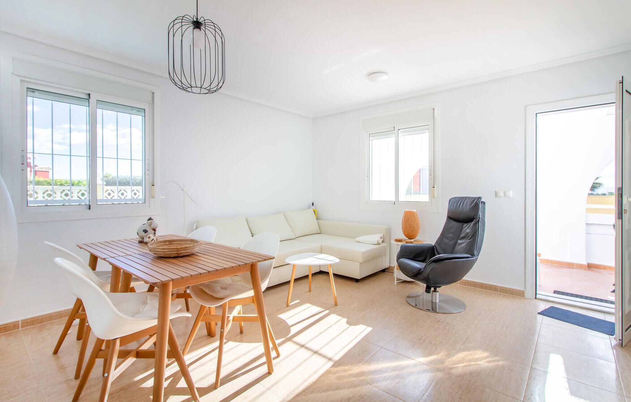 Un salon lumineux et moderne, avec une table à manger en bois, des chaises blanches, un canapé beige et un fauteuil en cuir noir.