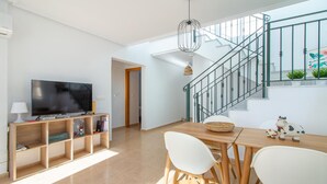 A modern living room with a flat-screen TV, wooden furniture, a staircase, and a view of the outdoors.