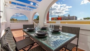 A dining area with a glass table and wicker chairs, overlooking a cityscape.