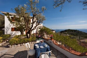 Une terrasse avec une table dressée pour deux personnes, offrant une vue sur un paysage côtier.