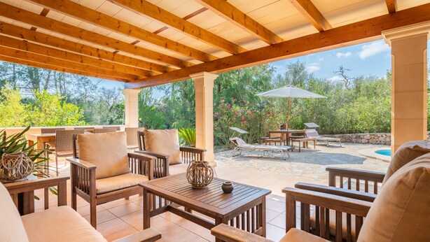 Un patio couvert am énagé avec du mobilier en bois, une table en pierre et une vue sur une piscine et un jardin.