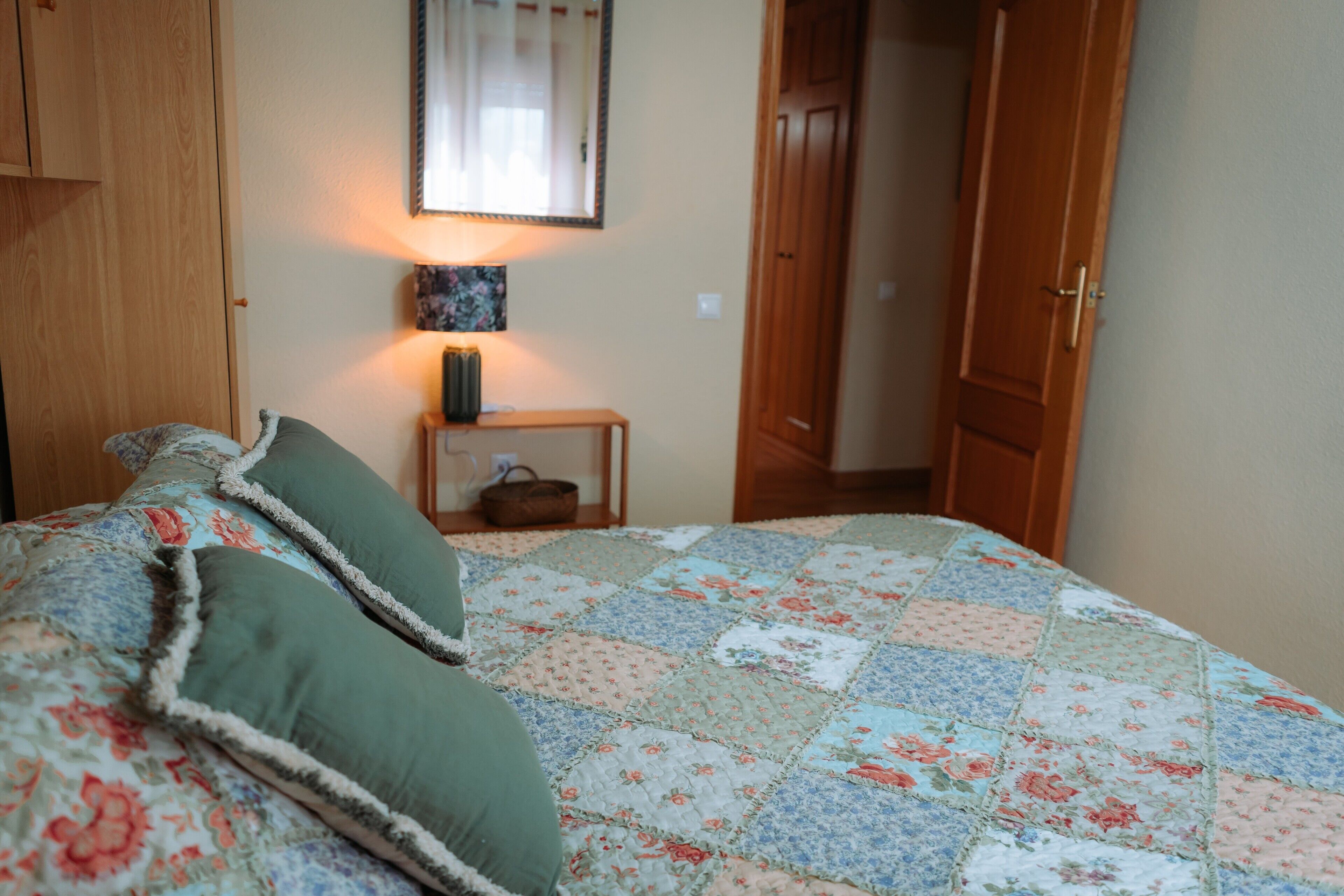 A bedroom with a quilted bedspread, a bedside lamp, and a wooden wardrobe.