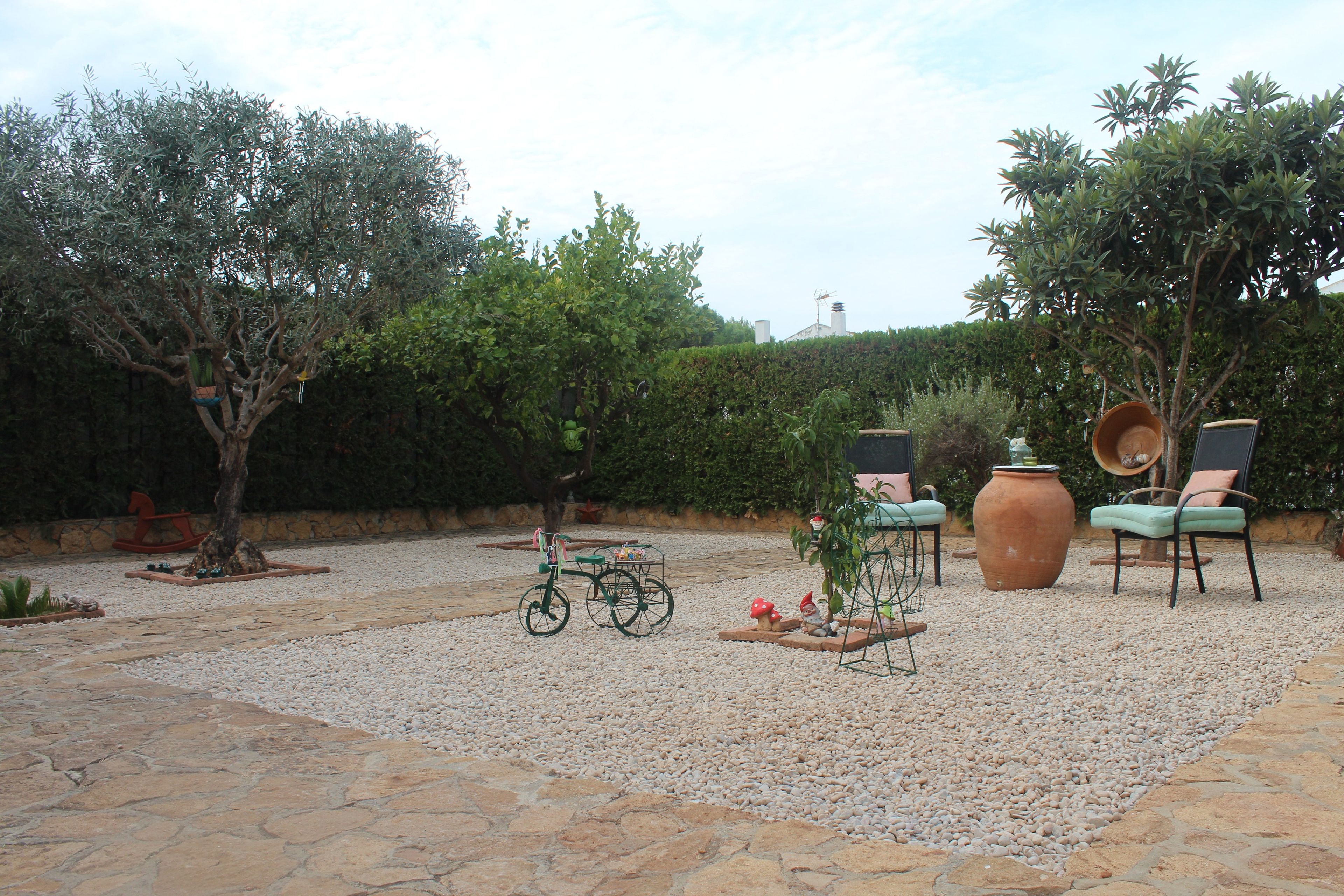 Un patio jardín con una bicicleta, una mesa, sillas y una maceta grande.