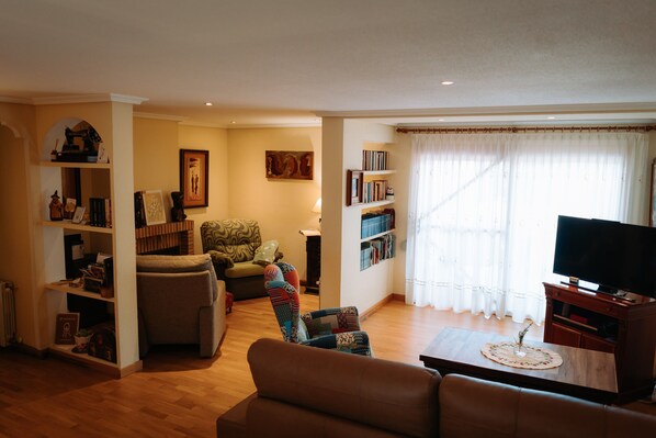 Una sala de estar con sofá, sillón, televisor, estantería y ventana con cortinas.