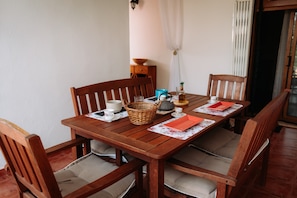 A wooden dining table with four chairs, a basket, a teapot, and a red napkin.