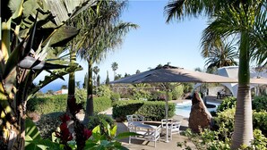 A poolside area with white chairs, a large umbrella, and a view of the ocean.